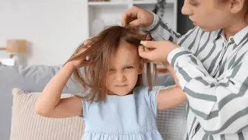 Zastanawiasz się, czy po kuracji na wszy dziecko może iść do przedszkola? Mama sprawdza włosy córki, która wygląda na zniecierpliwioną.