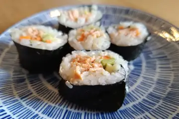 Pięć kawałków sushi z łososiem, ryżem i warzywami na niebiesko-białym talerzu.