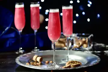Cztery kieliszki musującego, różowego drinka Boonekamp. Jak pić? Z orzeszkami i biszkoptami na srebrnej tacy.