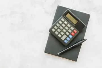 Kalkulator i długopis na czarnym notesie. Obliczanie, ile urlopu na pół etatu, to proste zadanie.