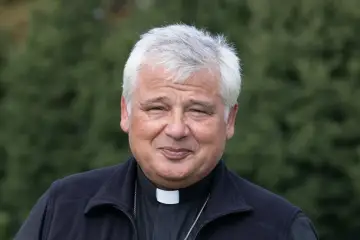 Uśmiechnięty mężczyzna w sutannie i czarnym bezrękawniku, z siwymi włosami. To jałmużnik papieski, który z troską patrzy na świat.