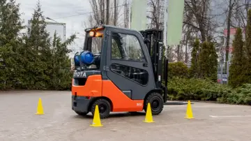 Pomarańczowo-szary wózek widłowy Toyota z butlą gazową, otoczony żółtymi pachołkami, gotowy do testów UDT.