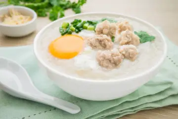 Miseczka pysznego congee z mięsnymi klopsikami, jajkiem i szczypiorkiem. Idealne na rozgrzewający posiłek.