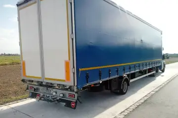 Tylna część niebieskiej naczepy z białymi drzwiami, stojąca na poboczu. To część zespołu pojazdów gotowego do drogi.