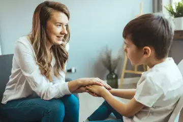 Kobieta i chłopiec trzymają się za ręce, wspierając się nawzajem. Może to symbolizować wydłużenie etapu edukacyjnego, gdzie wsparcie jest kluczowe.