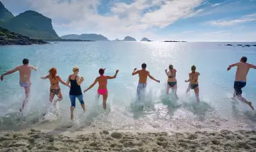 Grupa ludzi biegnie do wody na piaszczystej plaży. Zastanawiasz się, jakie ubezpieczenie turystyczne wybrać, by cieszyć się wakacjami bez obaw.