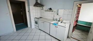 Kuchnia do remontu w Legnicy. Białe płytki, stara kuchenka i zlew. Idealne miejsce, by dowiedzieć się, jak dostać mieszkanie do remontu Legnica.