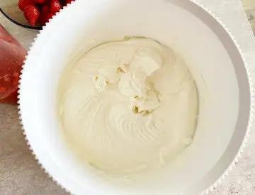 Gładka, kremowa masa z mascarpone w białej misie, gotowa do deseru. Obok miski widać miseczkę z truskawkami.