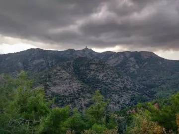 Góry Troodos pod burzliwym niebem. W oddali na szczycie widać charakterystyczną budowlę.