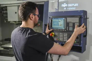 Operator CNC przy panelu sterowania maszyny. Dobra praca to wysokie operator cnc zarobki.