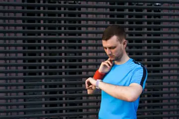 Mężczyzna w niebieskiej koszulce sprawdza pulsometr, ciesząc się niskim tętnem spoczynkowym po treningu.
