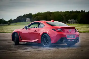 Czerwona Toyota 86 GR w poślizgu, z opon dymiących na asfalcie. W tle zielone pola i drzewa.