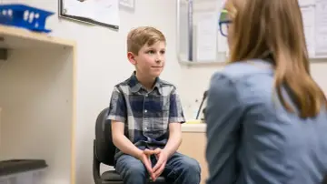 Chłopiec z ADHD siedzi na krześle, rozmawiając z terapeutką.