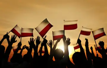 Tłum z polskimi flagami wzniesionymi ku niebu, symbol wolności i upadku komunizmu w Polsce.