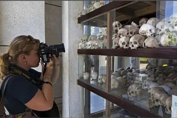Kobieta fotografuje ludzkie czaszki na wystawie upamiętniającej pola śmierci w Kambodży.