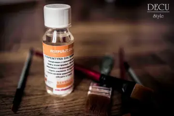 Butelka terpentyny balsamicznej i pędzle malarskie na drewnianym tle.