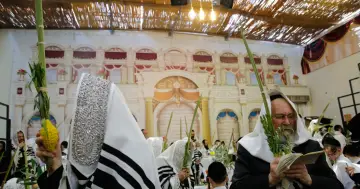 Mężczyźni w tradycyjnych strojach świętują Sukkot, trzymając gałązki i cytrynę. Obchody święta namiotów w synagodze.