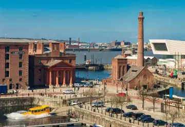 Albert Dock w Liverpoolu, gdzie jest? Żółty amfibia wjeżdża do wody, a w tle widać nowoczesne budynki i zabytkowe ceglane magazyny.