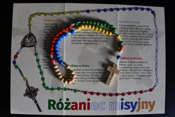 Kolorowy różaniec misyjny z drewnianym krzyżykiem i medalikiem, ułożony na kartce z modlitwami za różne kontynenty.
