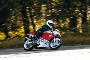 Motocyklista w kasku pędzi na czerwono-białym Suzuki RGV 250 przez leśną drogę.