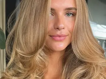 Kobieta z pięknymi, falowanymi włosami w odcieniu maślany blond. Jej zielone oczy i delikatny uśmiech dodają jej uroku.
