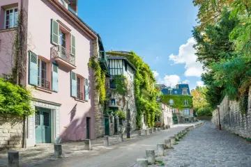 Urokliwa, brukowana uliczka w paryskiej dzielnicy le Marais, z pastelowymi kamienicami porośniętymi bluszczem.