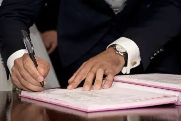 Mężczyzna w garniturze podpisuje dokument, co może oznaczać rozwiązanie umowy zlecenia za porozumieniem stron.