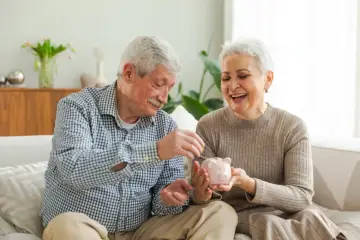 Szczęśliwa para seniorów wrzuca monety do świnki-skarbonki, planując spokojne przejście na emeryturę.