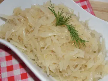Gotowana biała kapusta do obiadu, podana w białej misce, ozdobiona gałązką koperku.