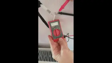 Jak sprawdzić kabel antenowy miernikiem? Ręka trzyma czerwony miernik, sondy dotykają odsłoniętych przewodów kabla.