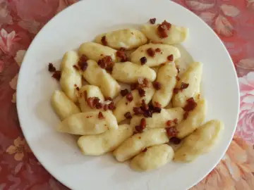 Kopytka z mąki ziemniaczanej, polane skwarkami z boczku, na białym talerzu.