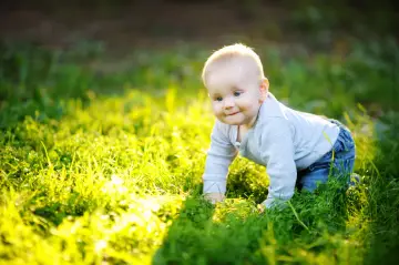 Uśmiechnięte dziecko na czworakach w trawie. Radość z adopcji dziecka w promieniach słońca.