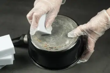Ręce w rękawiczkach czyszczą przypalony spód garnka gąbką. Czy pasta z sody i octu naprawdę działa na przypalony spód garnka?