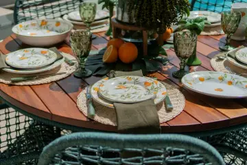 Oto inspiracja, jak udekorować stół na przyjęcie w ogrodzie w stylu boho: talerze z motywem cytrusów, zielone kieliszki i plecione podkładki tworzą letni klimat.