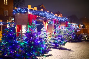 Magiczny jarmark świąteczny w Warszawie. Choinki ozdobione kolorowymi lampkami, drewniane budki i czerwone zasłony tworzą świąteczną atmosferę.
