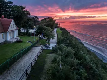 Zachód słońca nad morzem w Jastrzębiej Górze. Spacerowicze na klifie, domki i piękne, różowe niebo.