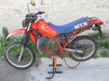 Pomarańczowy motocykl Honda MTX 125 z niebieskim siedzeniem, gotowy do jazdy po wertepach.