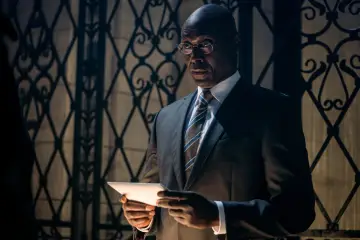 Winston z obsady John Wick, w garniturze i okularach, trzyma tablet.