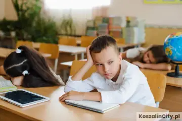 Zmęczony chłopiec z ręką na głowie siedzi przy ławce, jakby uczył się w szkole z czasów pruskiego systemu edukacji. Obok śpi koleżanka.