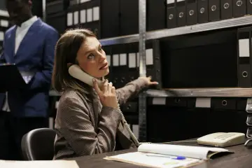 Kobieta, pracująca jako kryminolog, odbiera telefon w archiwum pełnym akt.