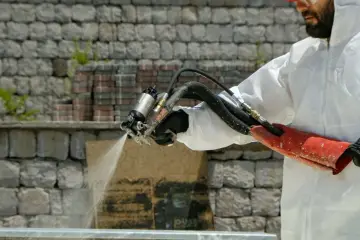 Un ouvrier en combinaison blanche applique une isolation mousse projetée sur un mur de pierres.