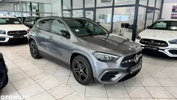 Szary Mercedes GLA 200 z czarnymi felgami stoi w salonie obok białego Mercedesa.