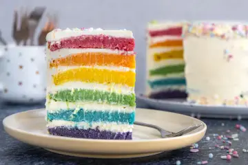 Ein Stück Regenbogen Kuchen mit bunten Schichten und Streuseln auf einem Teller.