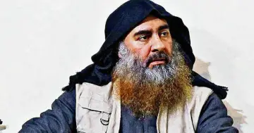 Mężczyzna z długą, siwiejącą brodą i czarnym nakryciem głowy, przypominający Abu Bakra al-Baghdadiego, siedzi w jasnym ubraniu.