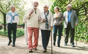 Grupa seniorów spaceruje po parku, ciesząc się świeżym powietrzem. Może rozmawiają o tym, jak przyjemnie jest płacić opłatę klimatyczną za takie widoki.