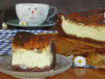 Pyszne izaura ciasto, kawałek na talerzyku, obok cały sernik i filiżanka z kotkiem.