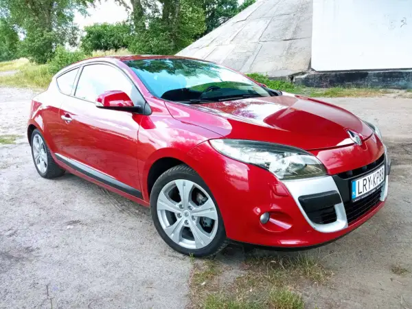 Czerwone Renault Megane Coupe 3 na tle betonowej konstrukcji i zieleni.