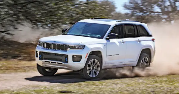 Biały Jeep Grand Cherokee z napędem 4x4 pokonuje piaszczystą drogę, wzbijając tumany kurzu.