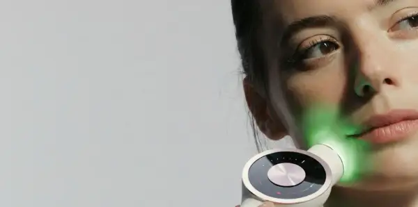 Une femme utilise un appareil de luminothérapie LED pour le visage, projetant une lumière verte apaisante.