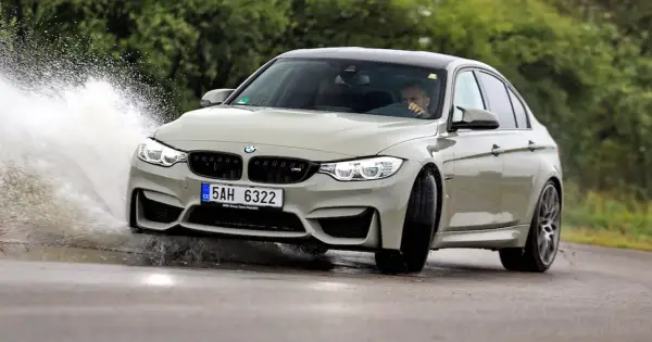 Szary BMW F80 M3 pokonuje kałużę, tworząc efektowny rozbryzg wody.